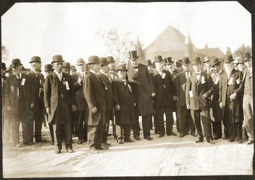 Chancellor Day with several members of the Japanese Commission, all in dark suits and hats. Campus buildings in the background