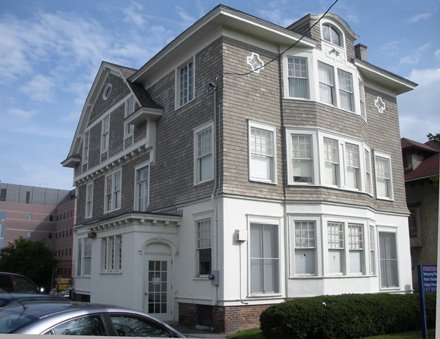 three story colonial house, bottom floor is white siding and top two floors are beige siding