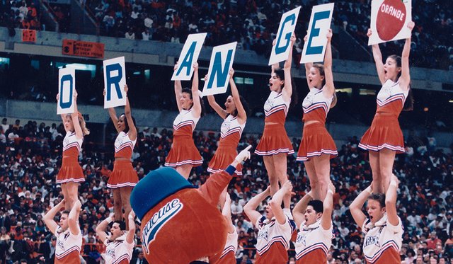 Archival photo of cheerleaders standing on other cheerleaders' shoulders in the Dome and holding signs that spell out "Orange" while being led by Otto the Orange