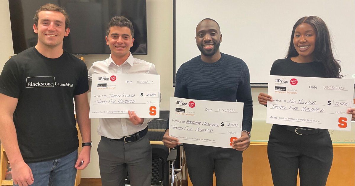 4 people standing holding giant checks
