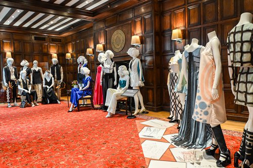 fashions on mannequins in formal room with wood paneling and orange carpet
