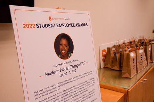Poster displayed at event in memory of former Libraries employee Madison Noelle Chappell ’19 with brown paper bags in background