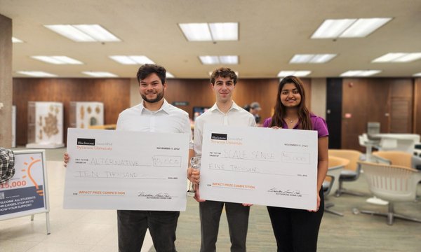 Ethan Tyo holding $10,000 oversized check on the left, Oliver Raycroft and Adya Parida holding $5,000 oversized check on the right