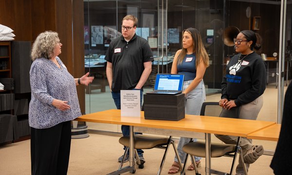 person talking to three students standing behind table