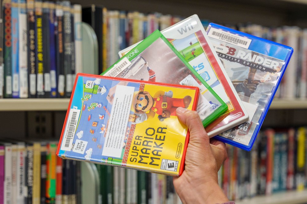 hand holding four different video games with shelves of DVDs in background