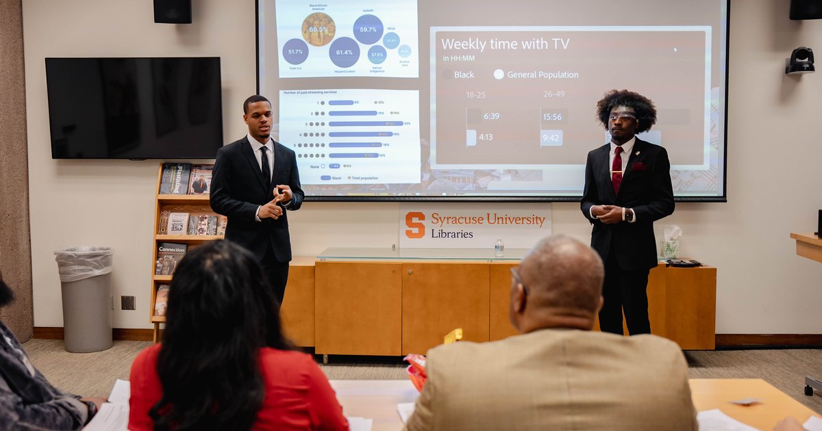 two black students in front of powerpoint pitch deck while judges watch