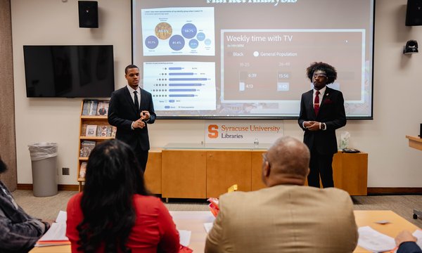 two black students in front of powerpoint pitch deck while judges watch
