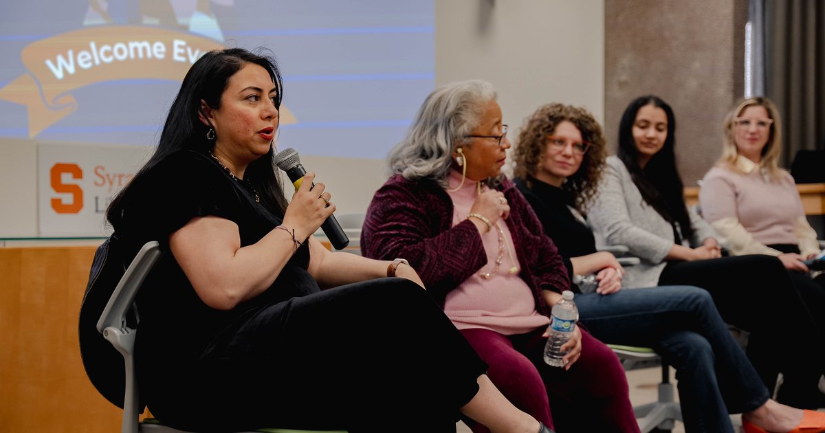 5 women sitting in front of room with one holding microphone
