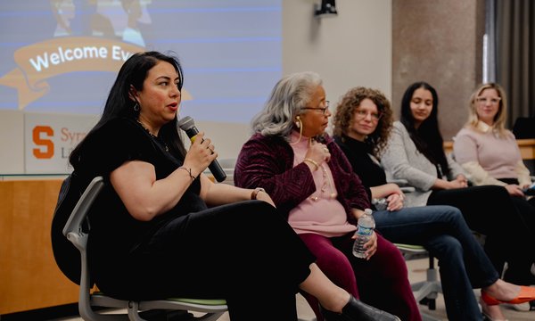 5 women sitting in front of room with one holding microphone
