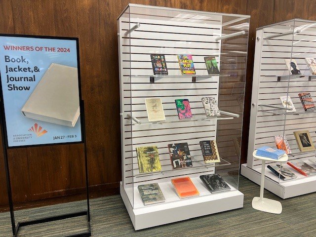 sign that reads "winners of 2024 Book, Jacket & Journal Show" next to display cases