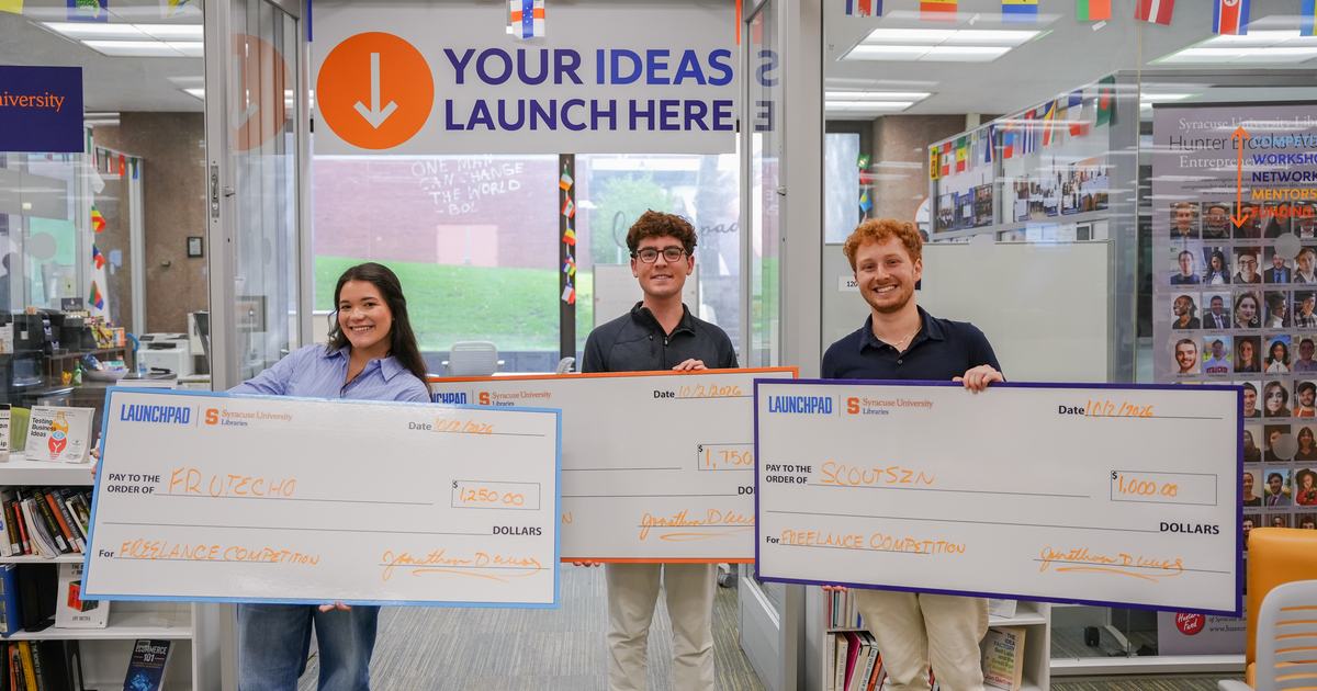 three people holding large oversized checks in front of LaunchPad space