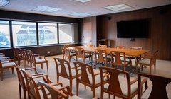 long wooden long table in front of room, setup panelist style, with rows of chairs in back of room