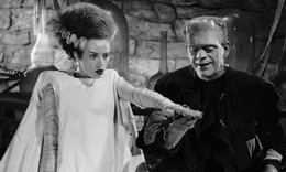 woman wearing white gown, hair sticking up and extending hand out next to Frankenstein monster wearing all black in Bride of Frankenstein