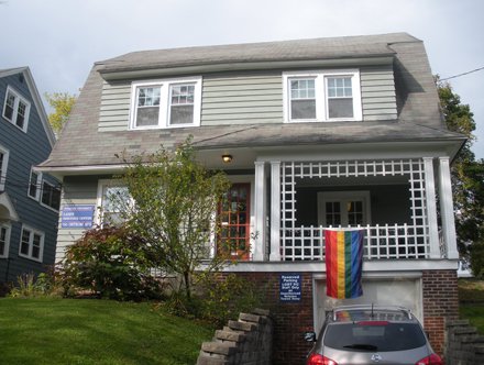 gray colonial two story house with rainbow flag hanging off porch