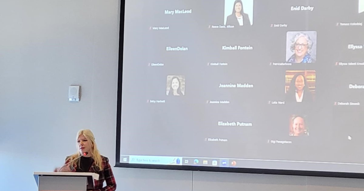 person at podium with screen behind them, attendees at table