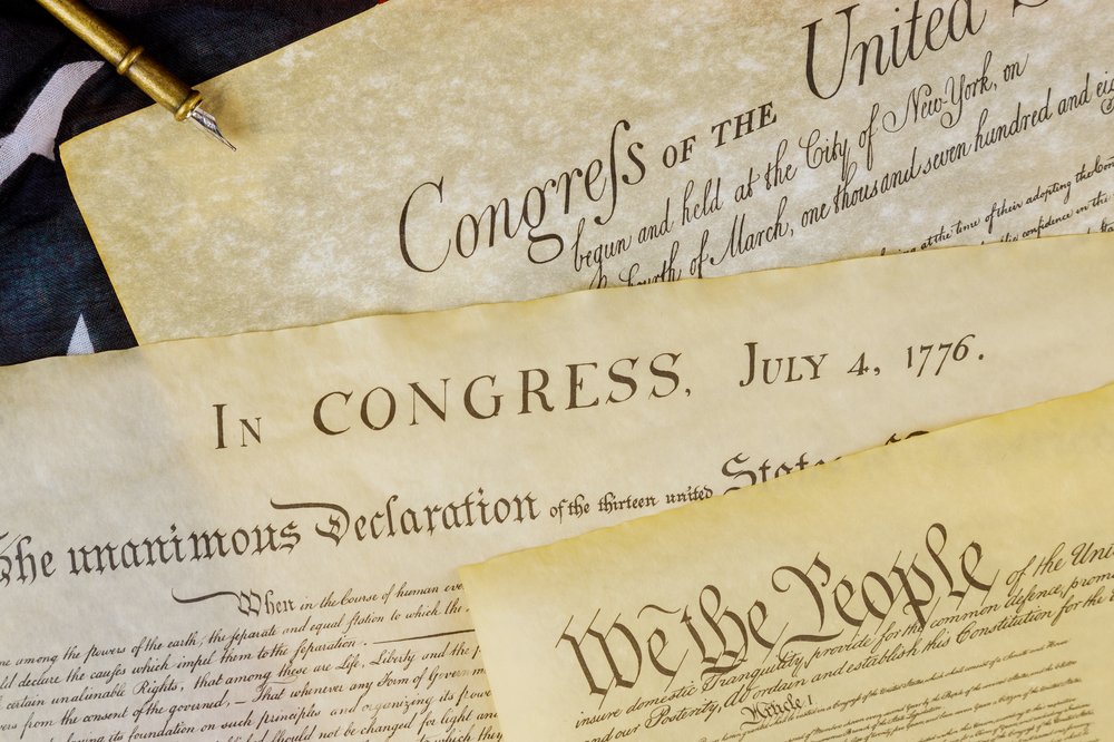 constitution document that reads "We the people..." and American flag behind it