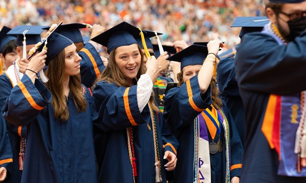Crowd of graduates in navy blue caps and gowns turning their tassels from one side to another