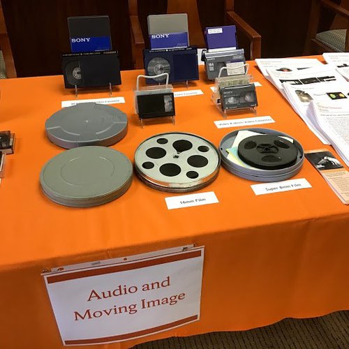 Film reels and VHS tapes on top of an orange covering of a table.