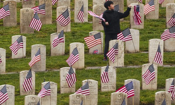 boy in cemetery with flags in front of graves