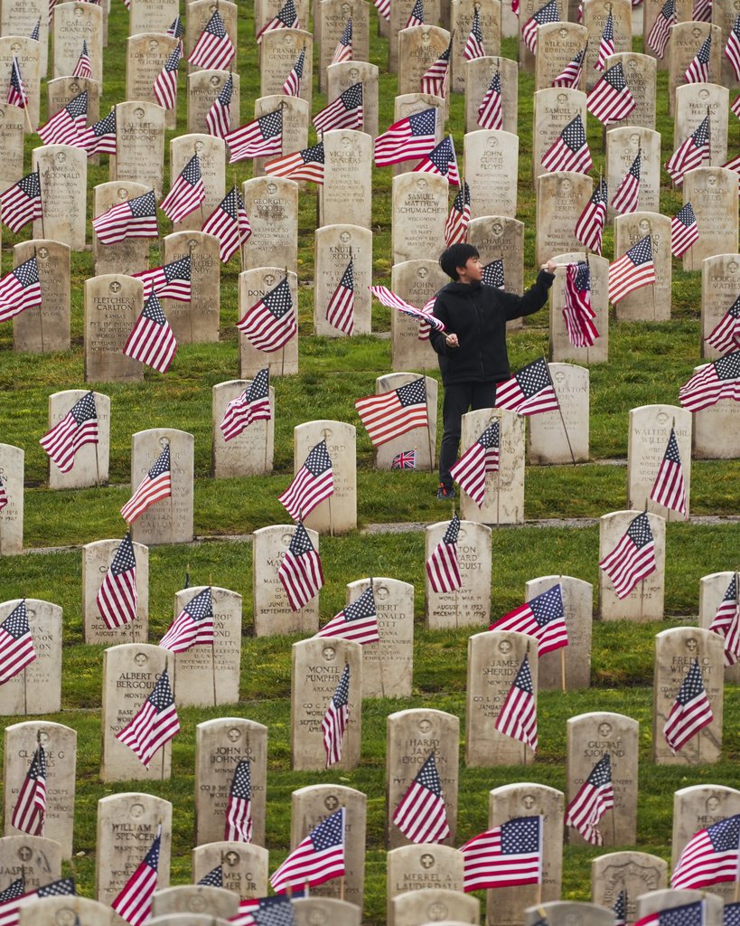boy in cemetery with flags in front of graves