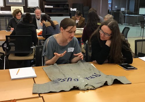 Two workshop participants examining a gray Syracuse University baseball uniform with Syracuse written on it in dark blue.
