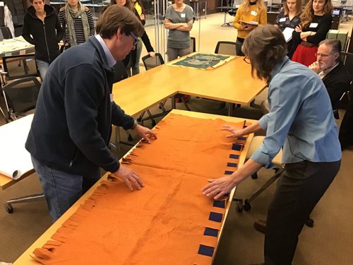 Conservator David Stokoe and Deborah Lee Trupin prepare an orange and blue banner for rolling by laying it out on a table..