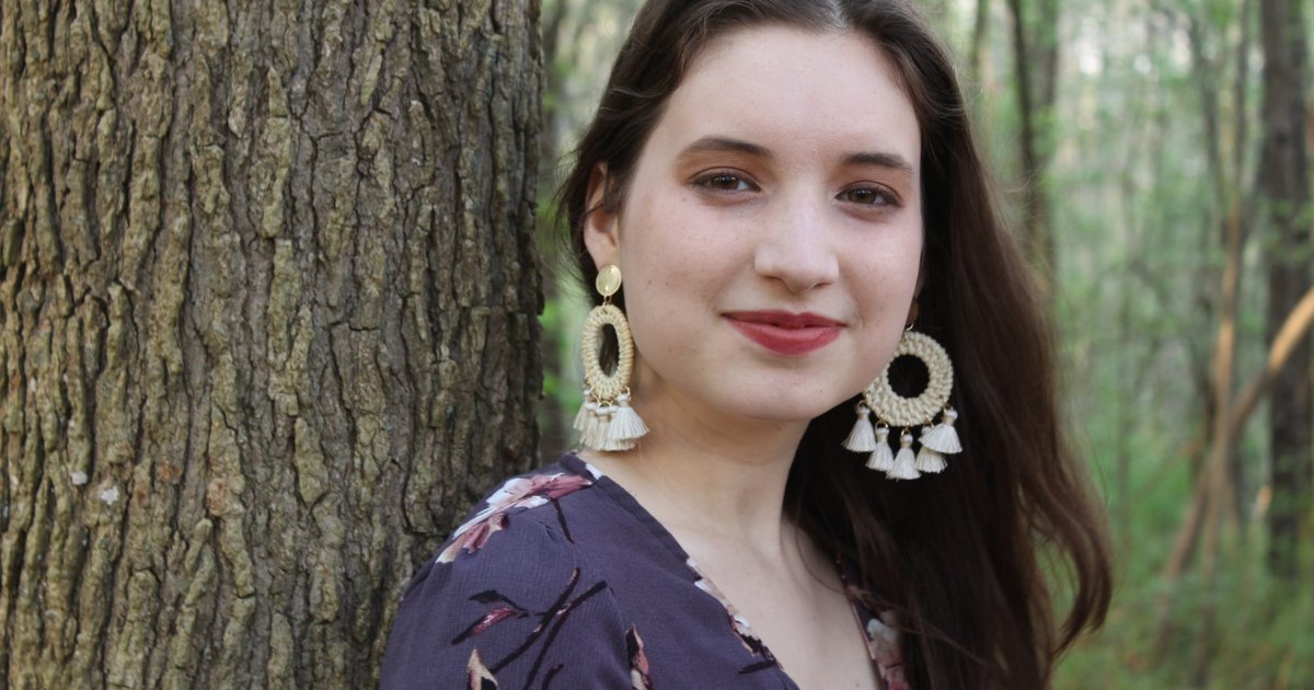 young woman standing against a tree