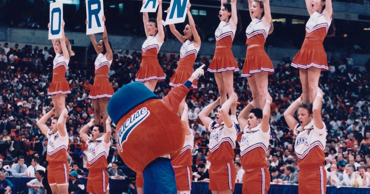 Otto the Orange standing in front of Syracuse Cheerleaders standing on shoulders and holding letters that spell the word Orange
