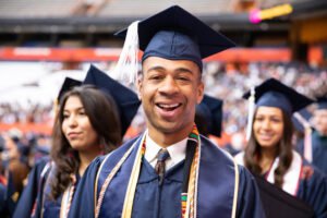 black man in cap and gown with other graduates behind him