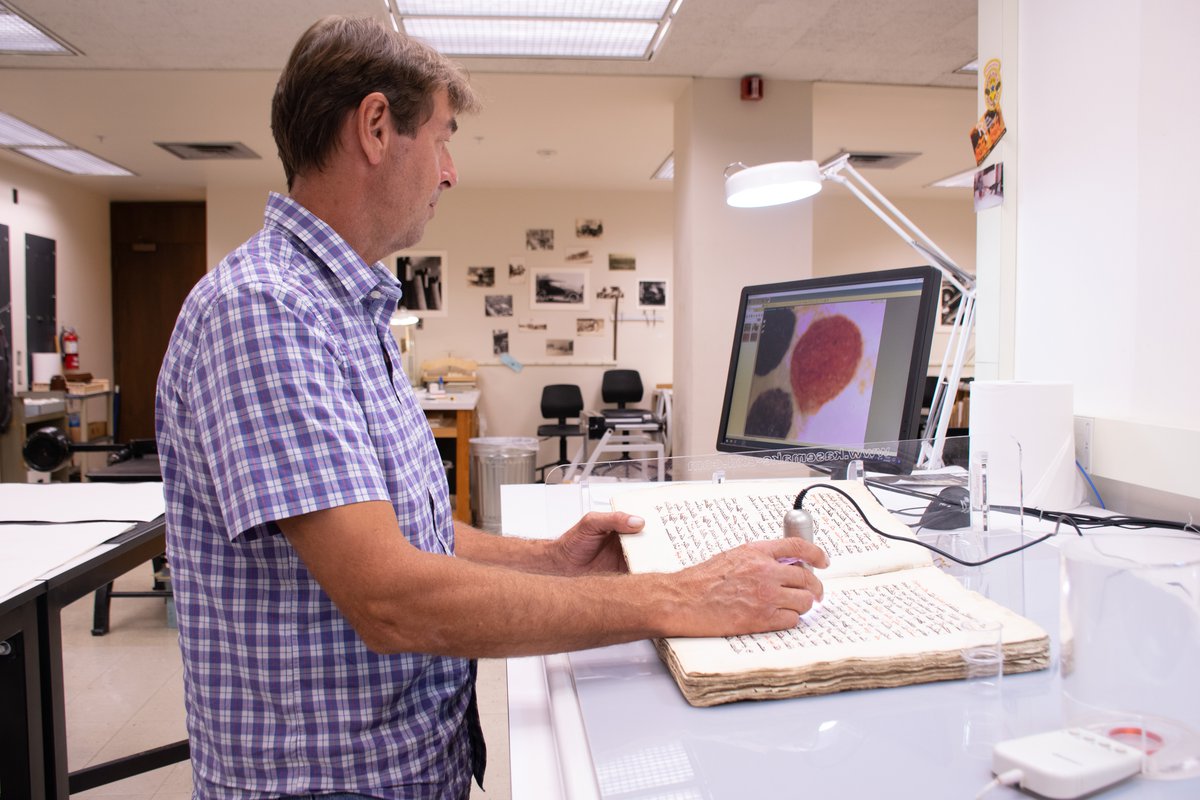 man working on booklet with software scree on desk