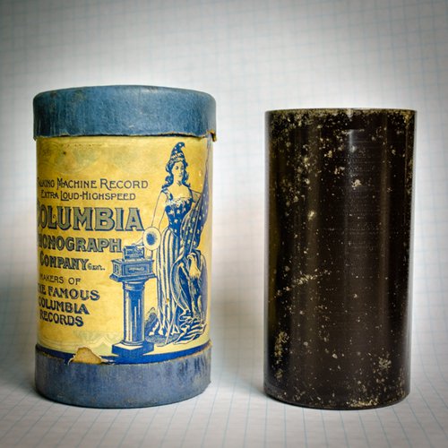 One blue and yellow and one black wax cylinder on top of graph paper.