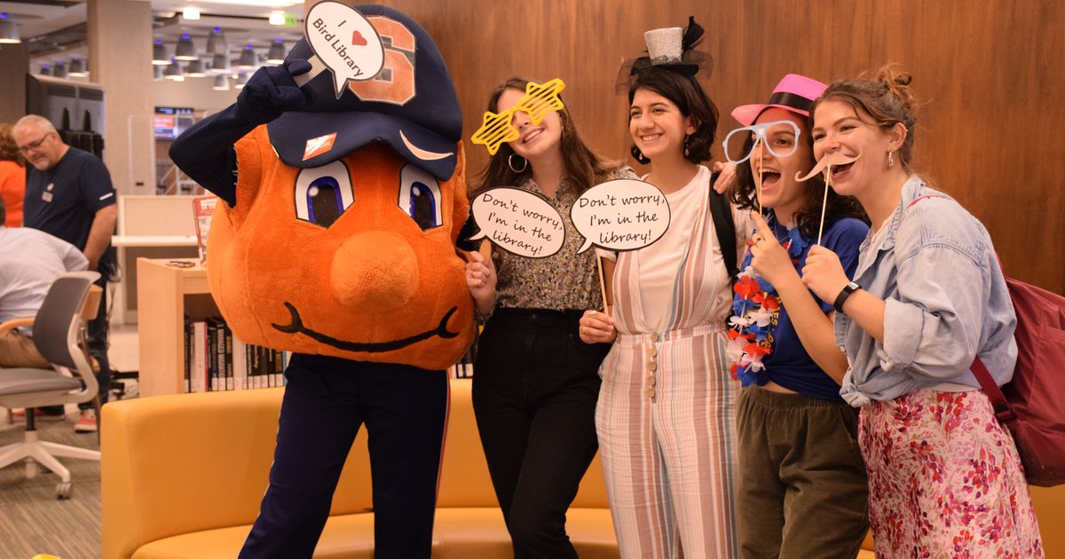 Students posing with photo booth props and Otto the Orange at welcome fest in Bird Library