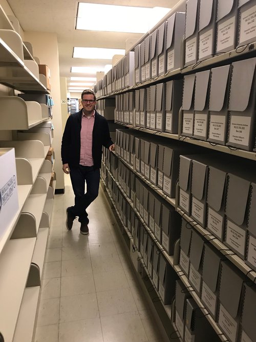 man posing in aisle with shelves of boxes on right