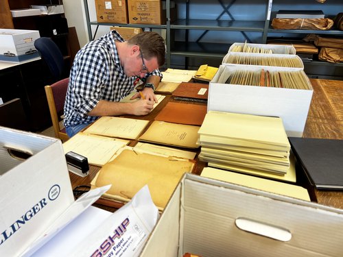 Dane working at table with boxes and piles of papers