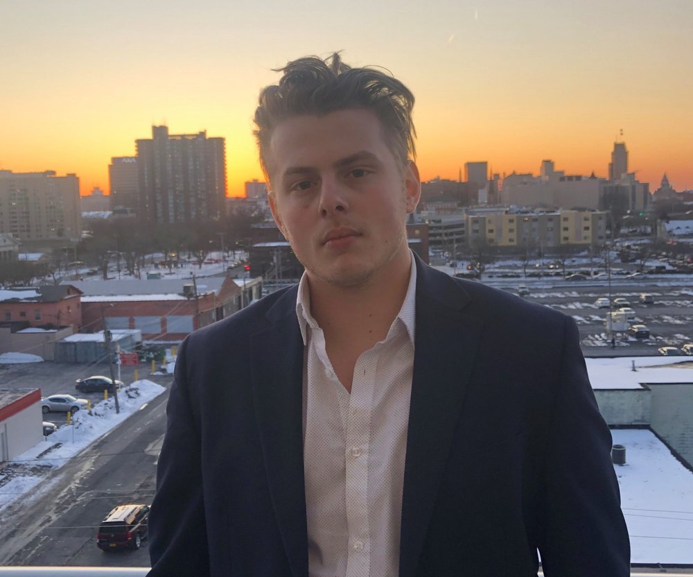 man pose for a photo with buildings and sunset in the background