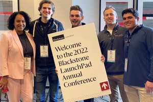 person in pink suit next to four men holding sign "Welcome to the 2022 Blackstone LaunchPad Annual Conference"