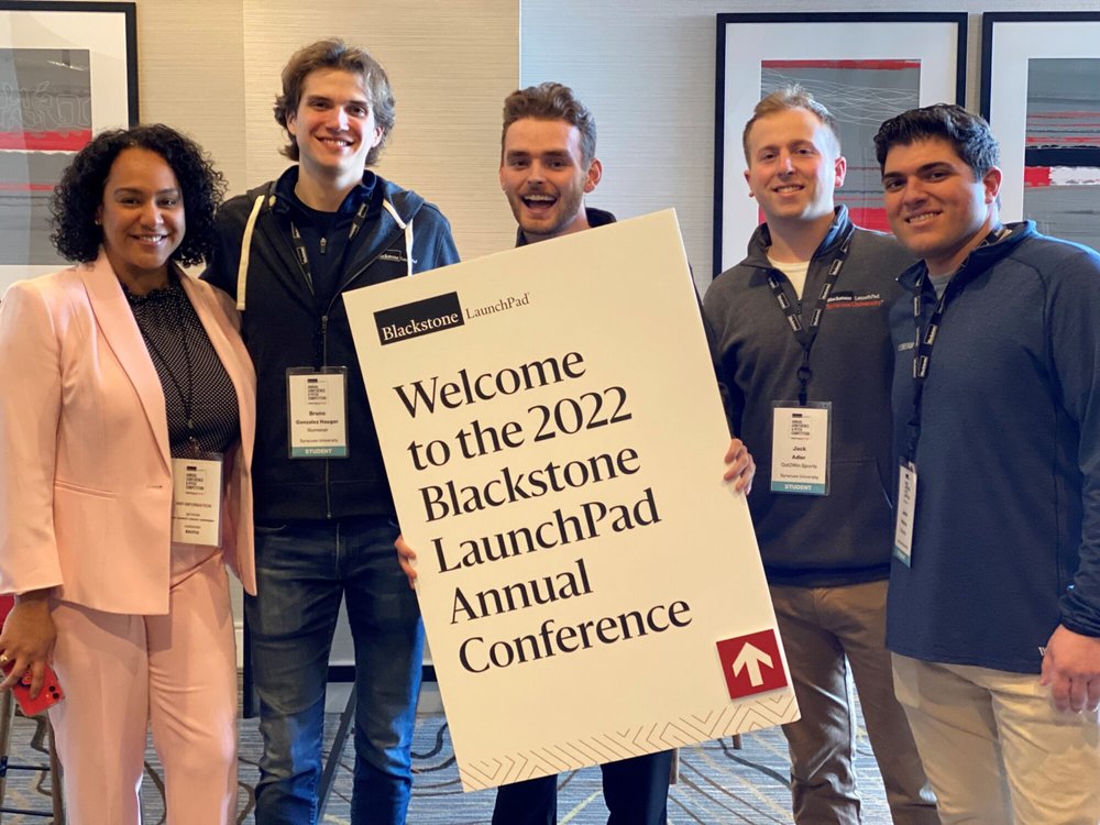 person in pink suit next to four men holding sign "Welcome to the 2022 Blackstone LaunchPad Annual Conference"