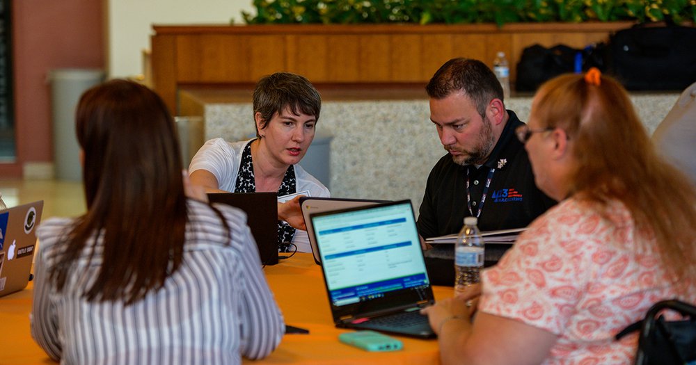 group of people sitting at table, one person at computer