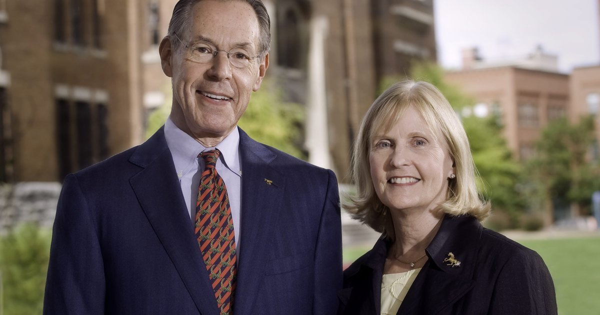 man and woman, both in suits, side by side with building in background