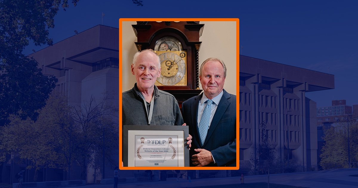 two people standing holding certificate in front of grandfather clock