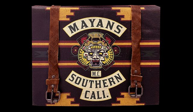 Brown case with leather straps and yellow details with name "Mayans M.C. Southern Cali" in banners with illustrated crest of a Mayan god in the center