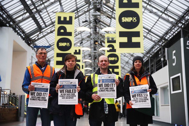 four people standing side by side holding up newspapers with different titles