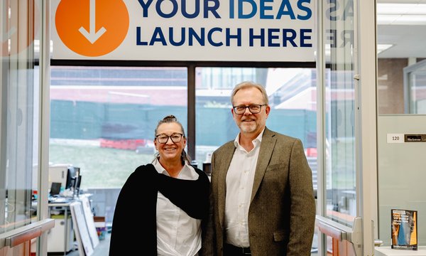 two people standing side by side in front of sign that says "Your Ideas Launch Here"