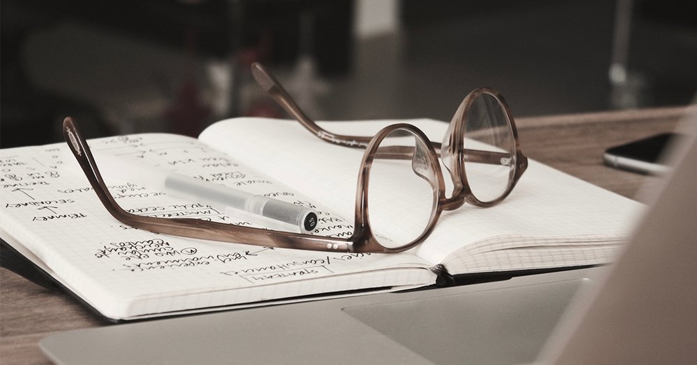 Pen and glasses sitting upside down on a notebook with writing in black pen