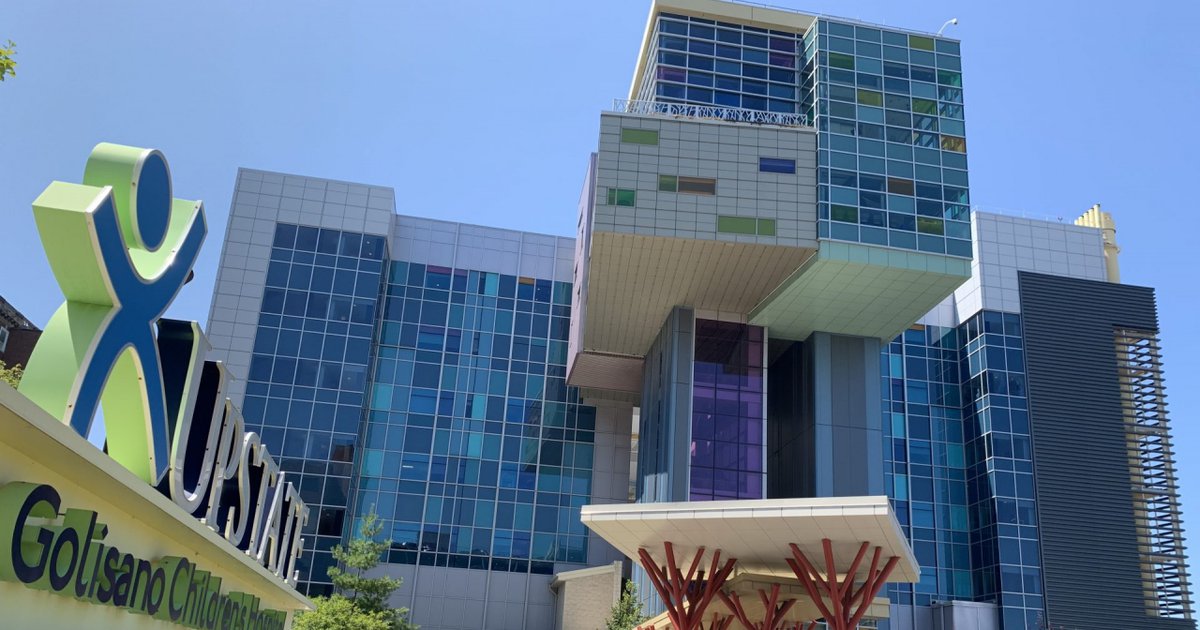 Exterior of Upstate Golisano Children's Hospital with green sign, tall buildings with blue window panes, and red sculptural entrance