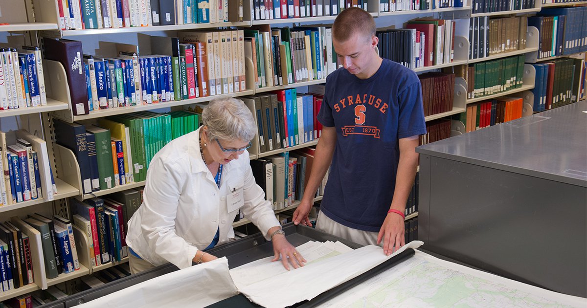 Library staff person helps student with government documents and maps collection at large table in front of bookshelf