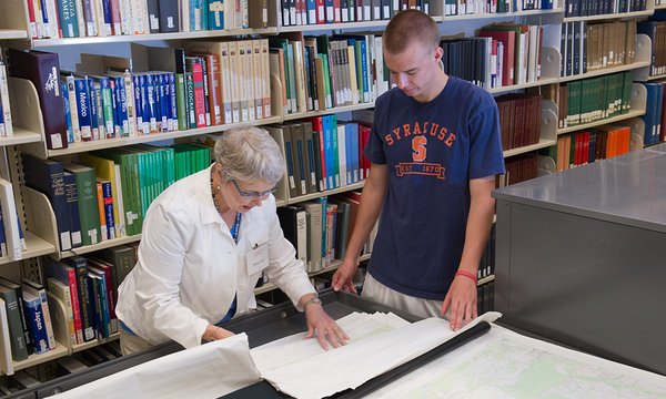 Library staff person helps student with government documents and maps collection at large table in front of bookshelf