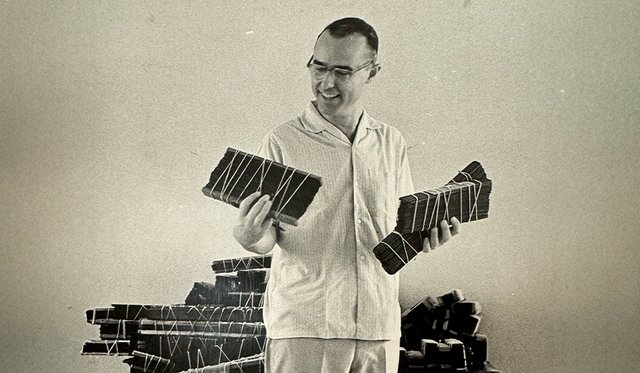 Sepia toned photo of H. Daniel Smith in white button up and glasses holding long pieces of wood wrapped in string