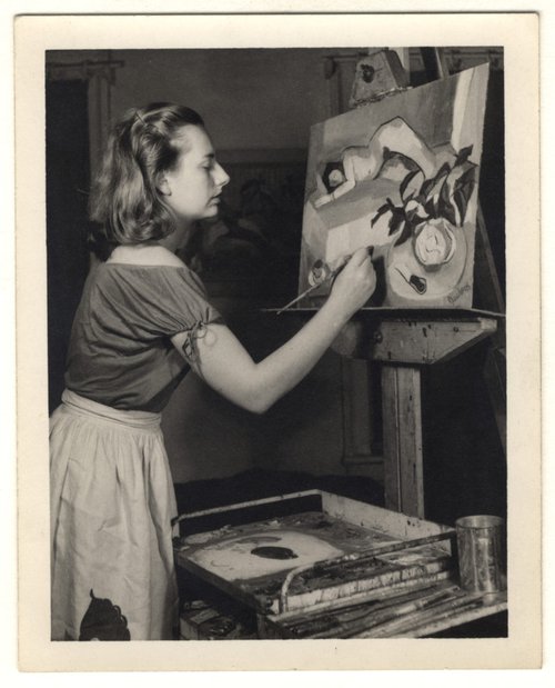 A woman painting a figural scene on canvas placed on an easel.