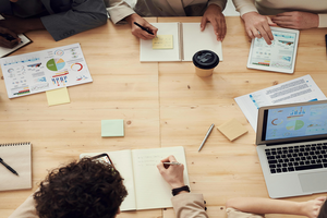 A group of researchers with laptops and documents around a table collaborating on a project.